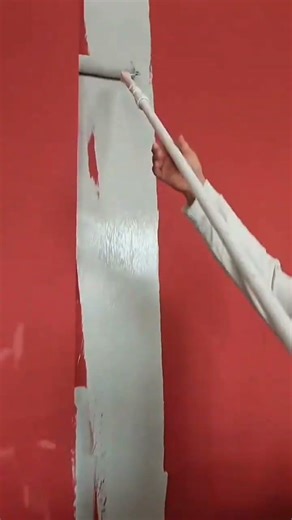 Roller applying light gray paint over red wall