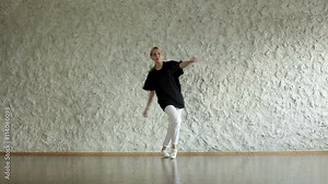 Young hip-hop and house female dancer performing against a light wall in the dancing hall