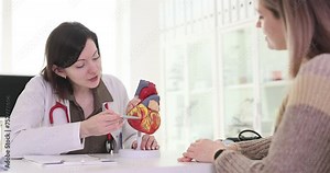 Doctor cardiologist showing structure of human heart to patient on model in clinic 4k movie slow motion. Diagnosis and treatment of heart defects concept