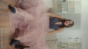 Vertical view. Angry Young Woman in a Festive Dress, Crying Sitting on the Sofa. A Nervous Woman with a Bottle is Wiping Tears, Feeling Heartbroken. Party, Graduation, Date. Concept of Social Life.
