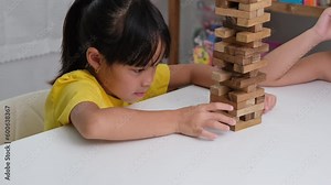 Cute Asian siblings having fun playing Jenga together. Two children playing Jenga board game on table in room at home. Wooden puzzles are games that increase intelligence for children.