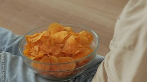 Girl Eating Chips From Bowl While Sitting on Floor in Living Room. Female Eating Unhealthy Potatoes Crisps. Snack on Junk Food. Child Eats Fast Food, Junk Food at Home Watching TV. Childhood Obesity.