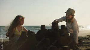 Children building castle from sand on beach. School-age boy and girl playing with sand in late afternoon sun. Summer at seaside.