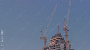 Skyscraper under construction with cranes timelapse. Building of new multi-storey tall tower with builders working on top