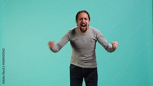 Portrait of irate man feeling outraged, yelling at friend, releasing pent up emotion, studio backdrop. Furious person full of rage screaming at mate isolated over blue studio background, camera A Stock Video
