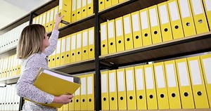 Woman secretary taking out yellow folder from top shelf of bookcase in office 4k movie slow motion