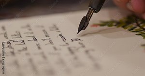 man writes Love letter with calligraphy and beautiful gothic letters. Old man with dirty hands writing a letter using a nib pen and ink or pigment from a pot in a low angle view across a wooden table.