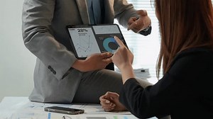 Business partners review charts and graphs on a digital tablet, discussing performance metrics and market trends in a collaborative office setting