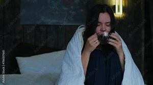 Woman warms herself with a cup of coffee while sitting in bed under a blanket. Girl drinking coffee or tea in bed