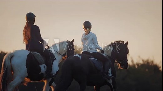 Two young girls horseback riding at golden sunset. Countryside activity with farm animals. Professional horse riders.