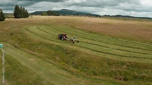 Tractor using mounted hay raking machine in preparation for baling, rotary tedder