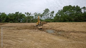Hydraulic excavator digging dirt from bottom of pond and moving it to top of side wall of pond at a land development site