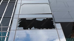 Broken window of a modern building as a result of an explosion blast wave. Sky reflecting in the remaining windows