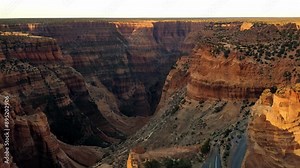 A canyon with a sunset in the background. The canyon is full of rocks and trees. The sun is setting behind the rocks, creating a beautiful and serene atmosphere
