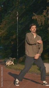 Man Dancing Contemporary Full Body At Sunset In Park 4K video. The man is surrounded by grass and trees. The camera moves behind the body and shows all the dynamics of the dancer. Slow motion dancing