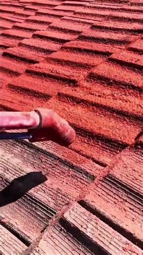 spraying bright red paint to restore the color of old roof tiles on a house under the bright sun