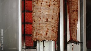 Close-up of rotating spit with meat sizzling on fire in open kitchen of Asian street cafe. Pan shot of pork near hot heating element being prepared for making shawarma and kebab without people.