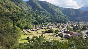 Shirakawa village, Gifu, Japan. A serene village nestled among lush mountains, surrounded by greenery and a clear sky, showcasing nature's beauty and tranquility.