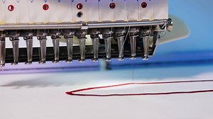 Automatic embroidery machine is working. Sewing machine needle in motion. Sewing machine needles with different colors moves up and down on white fabric. Close-up.