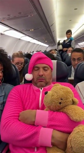 A middle aged man in an airplane cabin who has turned his economy seat into a be