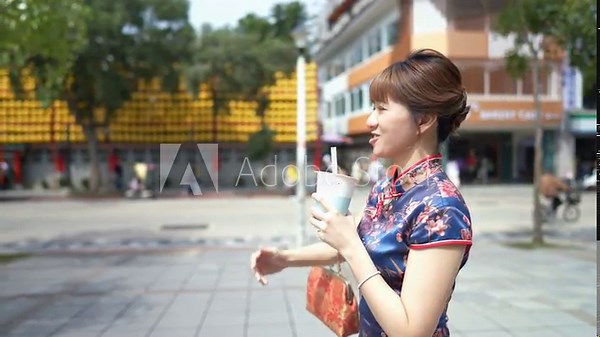 A young Taiwanese woman in a blue traditional cheongsam dress sips bubble tea while walking past historic buildings in Wanhua District, Taipei City, Taiwan. slowmotion