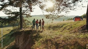 Company of young people hanging out outdoors on a high hill, observing the beauty of nature and enjoying beer. Having a picnic, hanging out together, spending time together. True friends