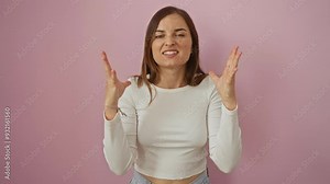 Young blonde woman standing with mad expression, shouting and yelling in frustration, arms raised in aggressive gesture, over isolated pink background