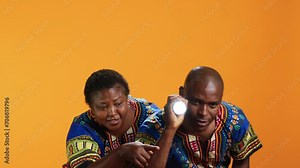 Confident man using flashlight to see what caused noise, trying to calm his wife who is hiding behind him. Terrified woman being anxious about weird sound, husband using lamp light and searching.