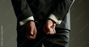 Business man in handcuffs behind back - close up on hands behind back as he turns to side profile