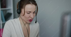 Woman receptionist wear headset consulting customer looking at computer talking with client in online computer chat, young female helpline operator secretary make conference video call.