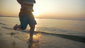 Barefoot kid running in sea water at sunset