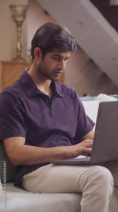Vertical Screen: Determined, Attractive Indian Man Engaged in Software Engineering Work from Home, Concentrating on Laptop while Sitting on Sofa. Coding, Debugging, Collaborating with Team Remotely