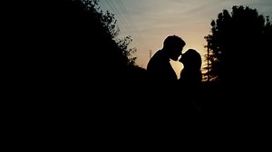 Silhouette of a bride and groom standing in front of each other and kissing
