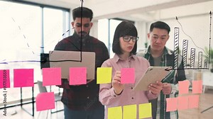 Team of young professionals brainstorming and collaborating using sticky notes on glass wall in modern office. Discussion focused on project planning, organization, and innovation.