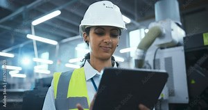 Female Worker in a White Hard Hat and Reflective Vest Standing in a Manufacturing Facility, Inspecting Machinery. Factory is Equipped with Advanced Automated Engineering Tools for Production Work