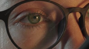 Camera zoom in womans eye in glasses looking at smartphone screen and surfing social media, monitor screen is reflected in the glasses. Work at night