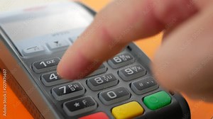 Hand of customer paying with contactless credit card with NFC technology on orange background. Credit card reader machine at bar counter with male holding credit card. Finger entering the PIN code