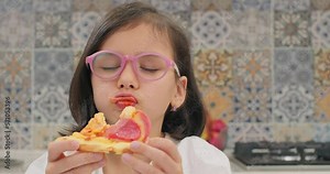 Cute girl enjoys eating pizza. Hungry girl eating a slice of pepperoni pizza with closed eyes. Eating with pleasure
