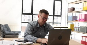 Tired male employee in glasses tries to type document on computer but falls asleep at table in office. Overworked man feels sleepy sitting at workplace