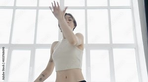 Attractive woman dancing at large window. Her silhouette highlighted against the bright backdrop. Room is minimalistic, with clean lines and sense of openness.