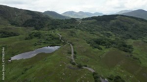 Aerial shot of the lush Ladies View in Ireland with a winding road and a pond, under overcast skies Stock Video