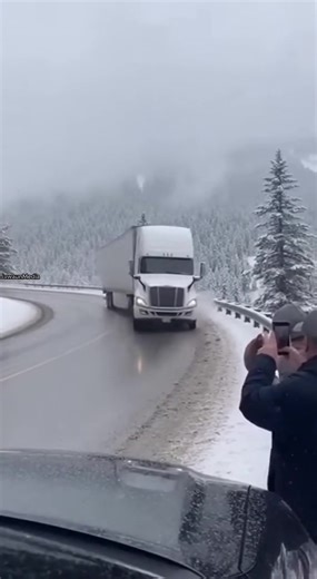 Icy Curve Sends Semi Truck Crashing Down Forested Slope ❄️ High-Elevation Highway — Colorado — Winter 2025 A routine winter drive turns chaotic when a semi-truck loses traction on black ice while navigating a snow-covered mountain pass. Shaky smartphone footage shows the truck sliding into the guardrail, which collapses before the tractor-trailer plunges down the embankment below. Snow and debris scatter through the trees as the trailer flips, leaving stunned bystanders watching in disbelief. Au