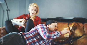 Woman Writing On Notepad While Man Playing with Dog At Home