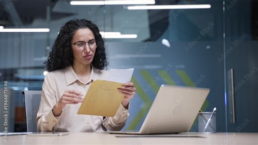 Disappointed businesswoman reading letter with bad news while sitting at workplace in business office. Upset female employee is depressed by unpleasant notification, shocked by information in document