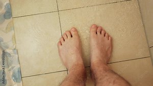 Caucasian male feet on a shower floor. Pouring water, top-down view, slow motion, camera movement