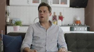 Portrait of sick man sneezing from allergy in slow motion.Young man with cold or allergic symptoms sitting on sofa at home sneezing.