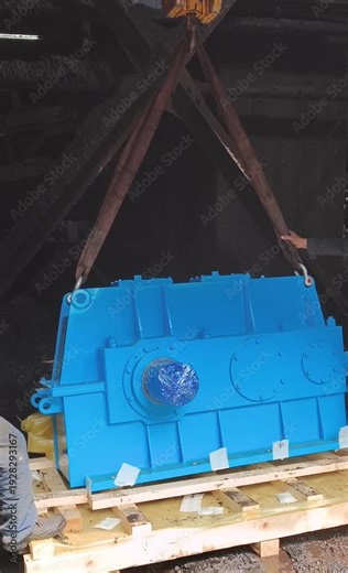 Heavy industrial gearbox being lifted using sling and rigging equipment during maintenance and replacement process. Mechanical lifting operation inside industrial plant area.