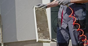 Worker cleaning a dirty air filter with a compressed air stream.