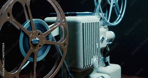 Old Movie Projector in Close up. Antique Movie Projector With 8mm Spinning Film Reels. Spinning Film Roll on a Vintage Film Projector. Light Beams From Film on an Old Projector