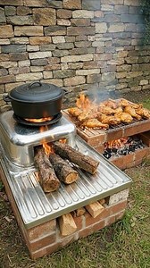 The Art of Cooking Over an Open Flame In a quiet outdoor corner framed by a rustic stone wall, this simple yet purposeful cooking setup brings tradition back to the forefront. Built from brick, metal, and wood, the outdoor stove embodies an age-old method of preparing food—one that values patience, fire, and craftsmanship over speed and convenience. At the heart of the scene, split logs feed a steady flame beneath a cast-iron pot. The fire crackles softly, its heat evenly distributed by the meta